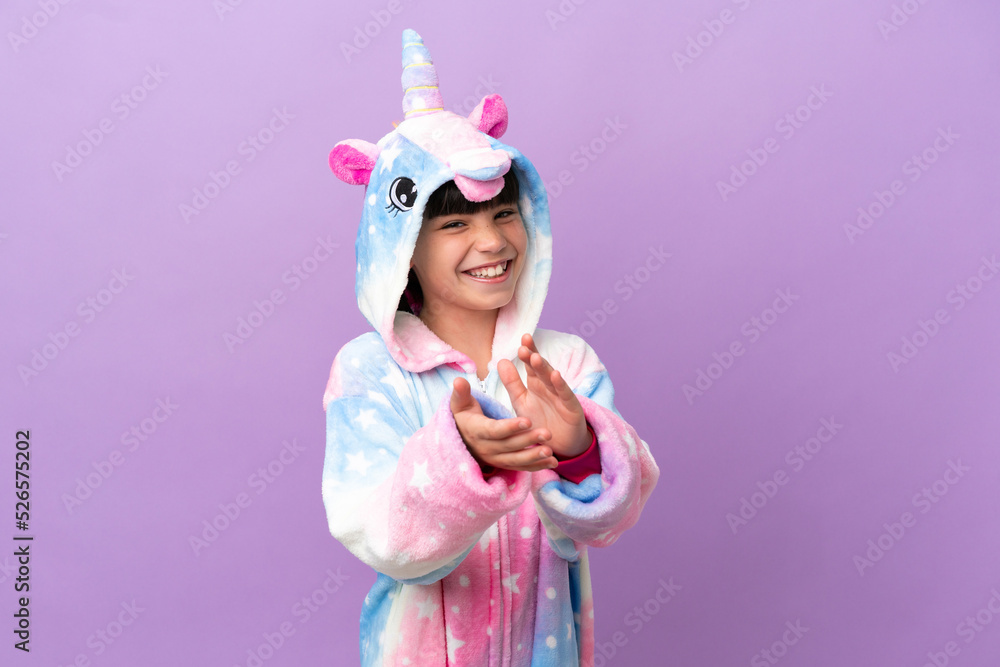 Little kid wearing a unicorn pajama isolated on purple background applauding after presentation in a conference Little kid wearing a unicorn pajama isolated on purple background applauding after presentation in a conference