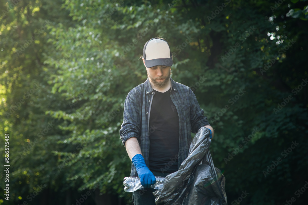 A young male volunteer cleans up bottles in the forest.