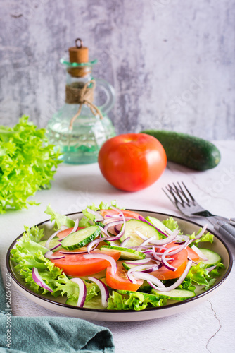 Salad of cucumbers, tomatoes and onions on lettuce leaves on a plate. Vegetarian food. Vertical view