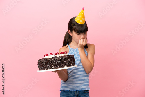 Little caucasian kid holding birthday cake isolated in pink background having doubts