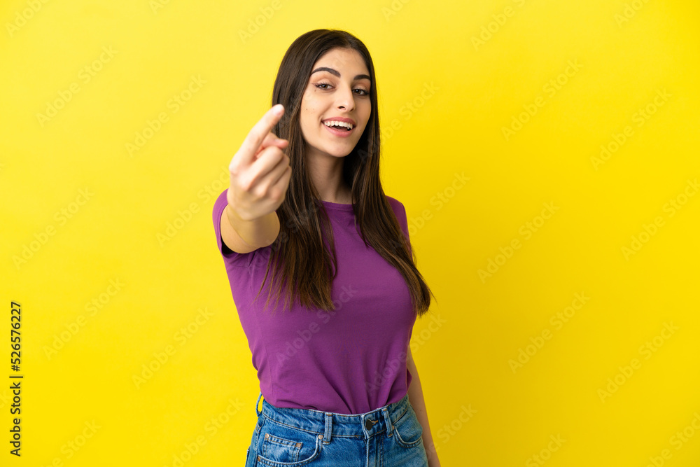 Young caucasian woman isolated on yellow background doing coming gesture Young caucasian woman isolated on yellow background doing coming gesture