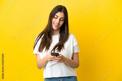 Young caucasian woman isolated on yellow background sending a message with the mobile