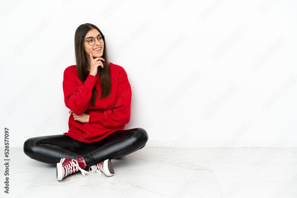 Young woman sitting on the floor isolated on white background thinking an idea while looking up Young woman sitting on the floor isolated on white background thinking an idea while looking up