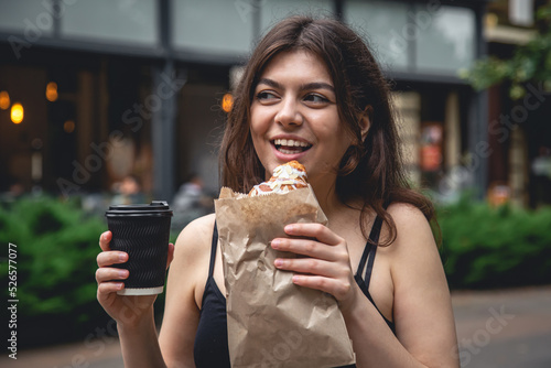 A young woman with a croissant and a cup of coffee on a city walk.