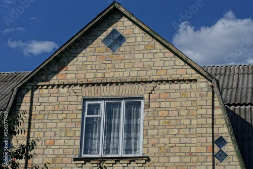 one big brown brick attic of a private house with a window against the blue sky