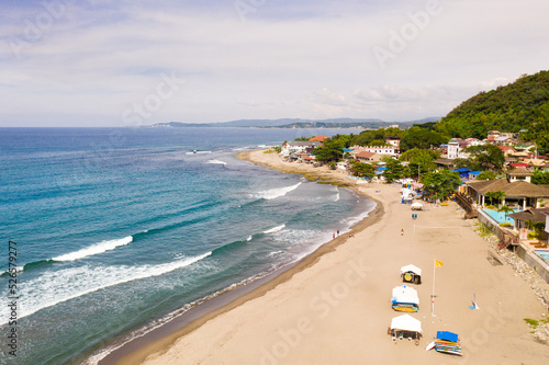 Sandy coast, buildings and blue sea with waves. San Juan, La Union, Philippines. The beaches of the Philippine Islands. Town near the sea.