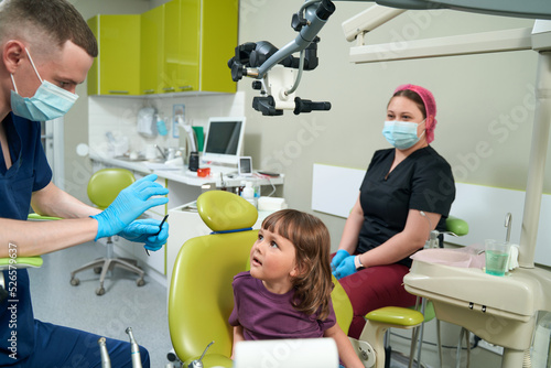 Pediatric dentist conversing with little girl before dental examination