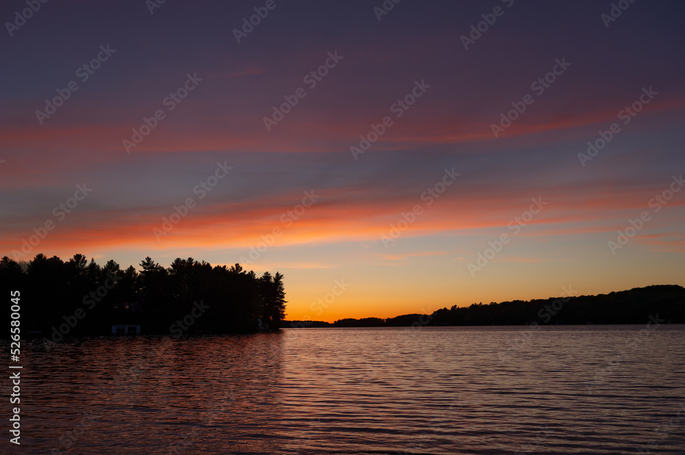 Beautiful sunset on a calm lake in Muskoka, in the sky the orange hues are visible.