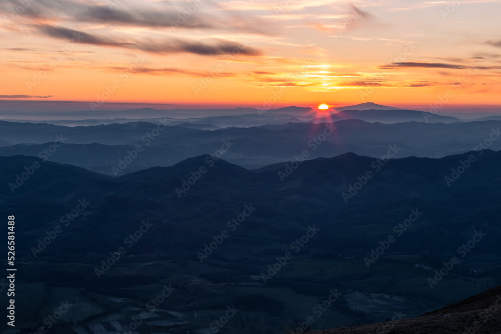 Distant sunset above layers of mountains and valleys with mist and fog