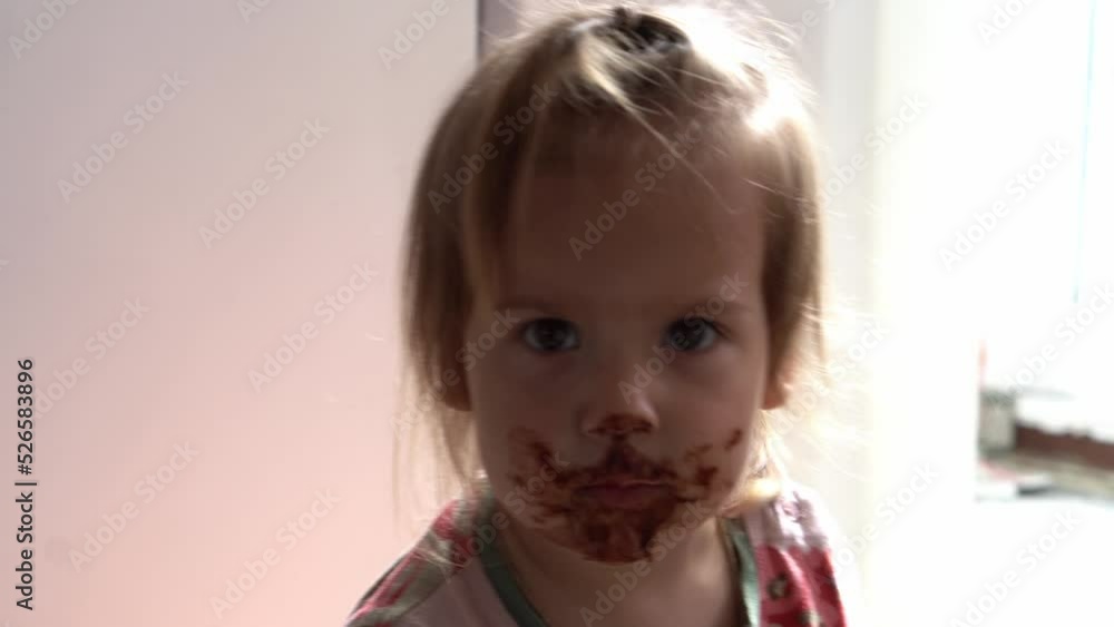 Close up baby dirty Face. Funny child eat chocolate. little toddler kid in the kitchen eating candy in the morning. happy family eats sweets girl dream concept. lifestyle cocoa confection.Childhood Close up baby dirty Face. Funny child eat chocolate. little toddler kid in the kitchen eating candy in the morning. happy family eats sweets girl dream concept. lifestyle cocoa confection.Childhood