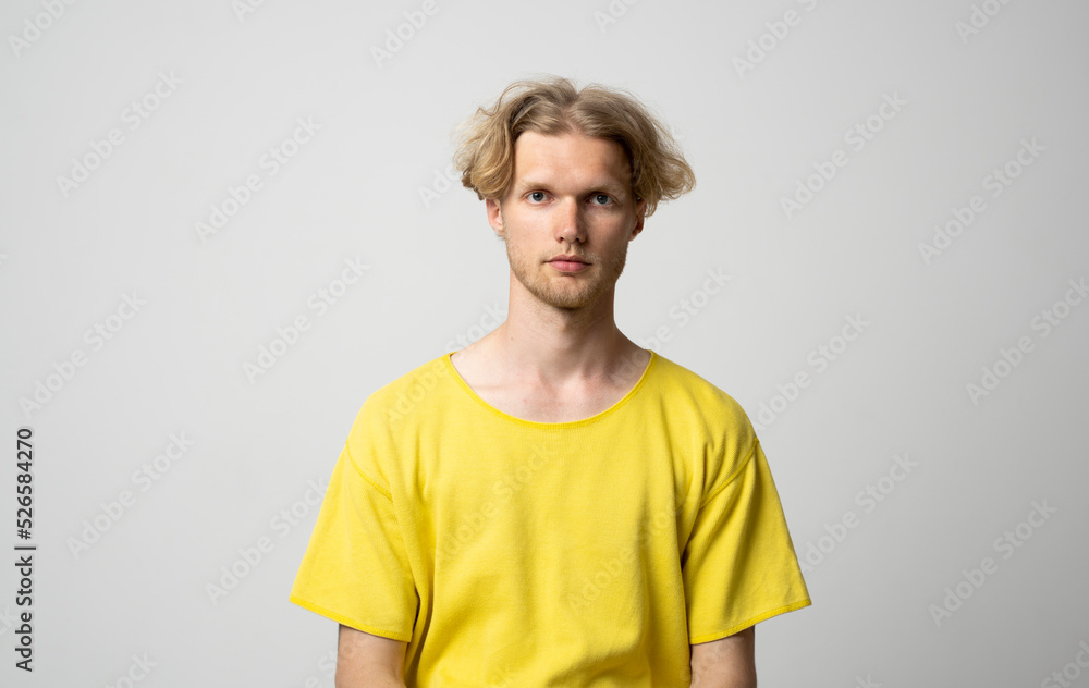 Portrait of calm serious mature young man without emotions. Beautiful emotionless guy in a yellow t-shirt looking to the camera, isolated over white background. Portrait of calm serious mature young man without emotions. Beautiful emotionless guy in a yellow t-shirt looking to the camera, isolated over white background.