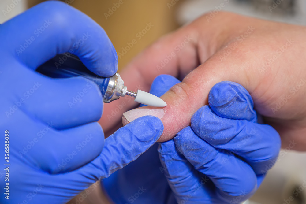 Manicurist master removing cuticles. Processing of rough cuticles and lateral folds of nails on hands with a conical instrument. Medical hardware manicure in a beauty salon Manicurist master removing cuticles. Processing of rough cuticles and lateral folds of nails on hands with a conical instrument. Medical hardware manicure in a beauty salon