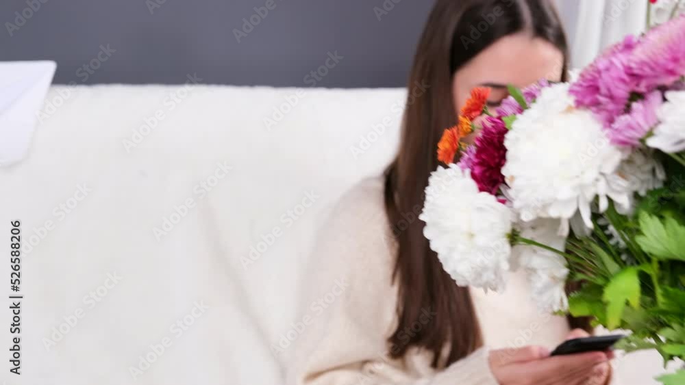 Attractive young girl sitting at home on the sofa and her boyfriend making a gift to her bouquet of beautiful flowers. Attractive young girl sitting at home on the sofa and her boyfriend making a gift to her bouquet of beautiful flowers.