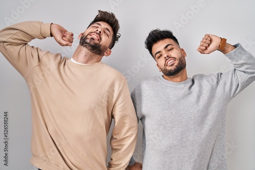 Young homosexual couple standing over white background stretching back, tired and relaxed, sleepy and yawning for early morning