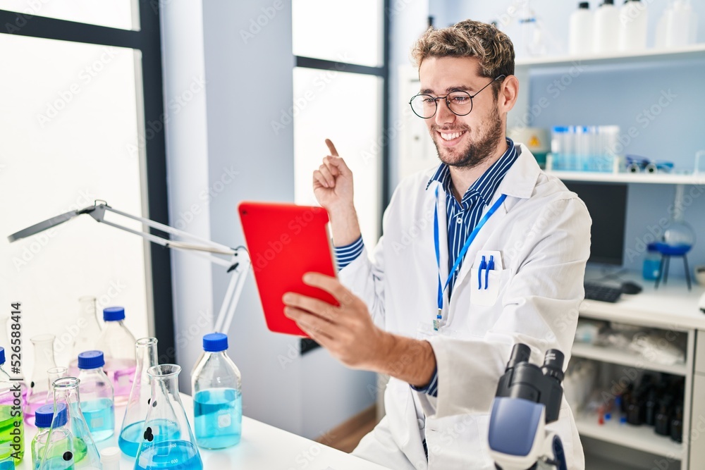 Hispanic man with beard working at scientist laboratory doing video call smiling happy pointing with hand and finger to the side Hispanic man with beard working at scientist laboratory doing video call smiling happy pointing with hand and finger to the side