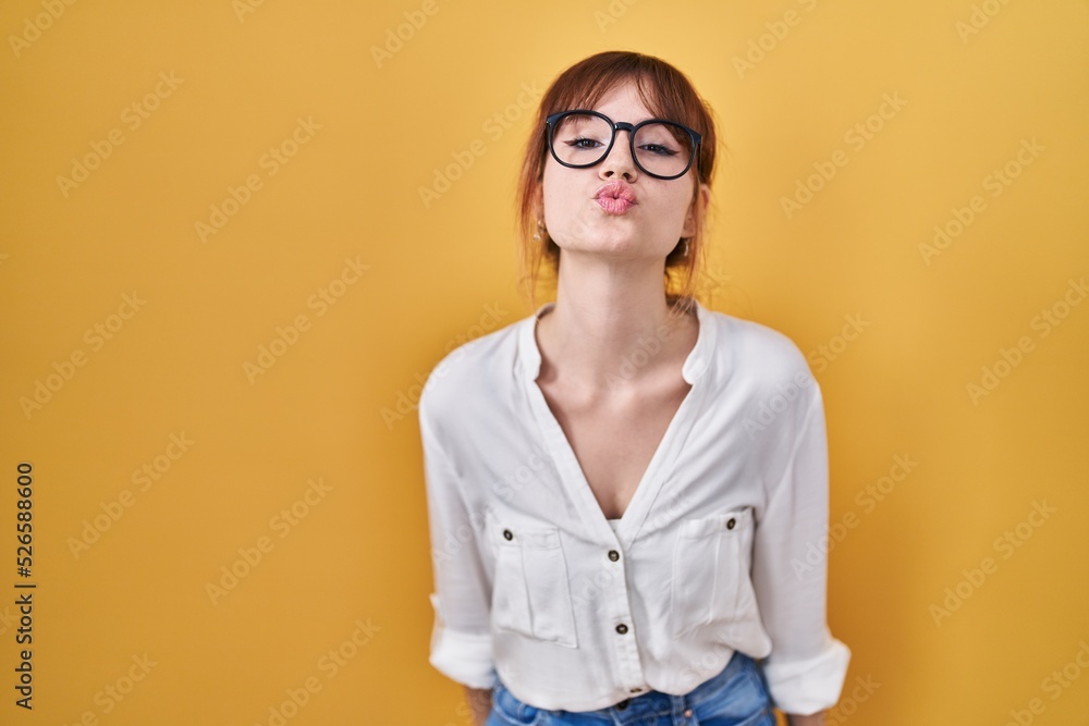 Young beautiful woman wearing casual shirt over yellow background looking at the camera blowing a kiss on air being lovely and sexy. love expression.