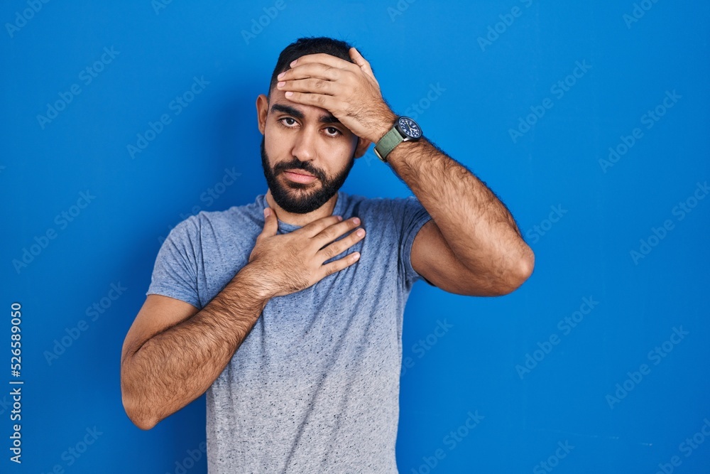Middle east man with beard standing over blue background touching forehead for illness and fever, flu and cold, virus sick Middle east man with beard standing over blue background touching forehead for illness and fever, flu and cold, virus sick