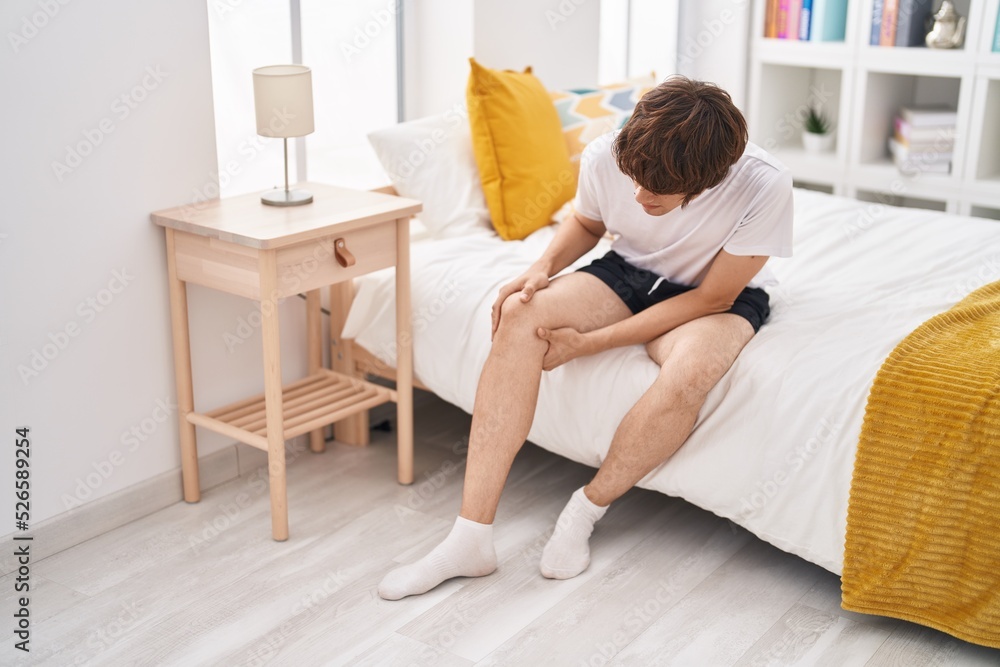 Young blond man suffering for knee injury sitting on bed at bedroom Young blond man suffering for knee injury sitting on bed at bedroom