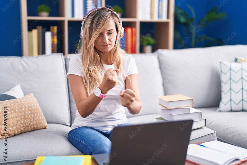Young blonde woman studying using computer laptop at home ready to fight with fist defense gesture, angry and upset face, afraid of problem Young blonde woman studying using computer laptop at home ready to fight with fist defense gesture, angry and upset face, afraid of problem