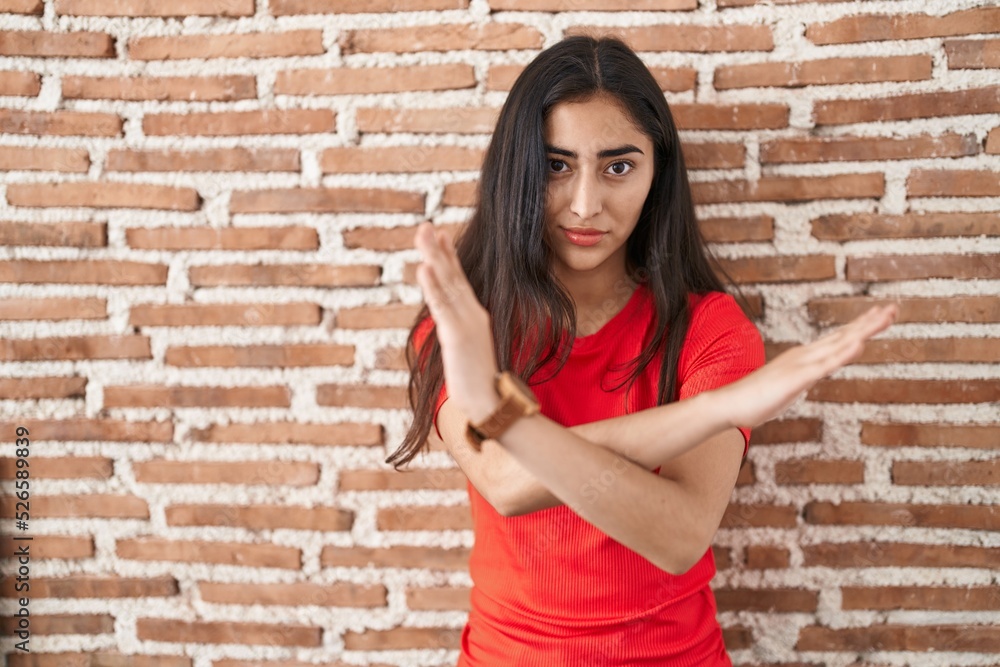 Young teenager girl standing over bricks wall rejection expression crossing arms doing negative sign, angry face Young teenager girl standing over bricks wall rejection expression crossing arms doing negative sign, angry face