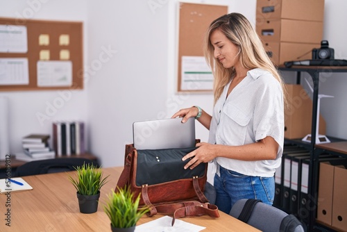 Young blonde woman business worker smiling confident holding laptop of briefcase at office photo