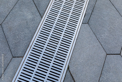 Metal storm sewer grate on shaped paving slabs in park. Drainage systems on paving slabs. Sidewalk construct.