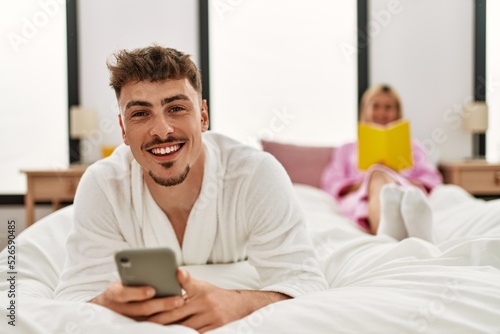 Young caucasian couple reading book and using smartphone at bedroom.