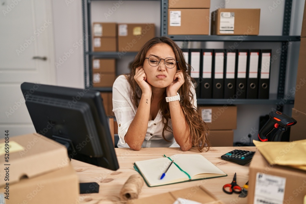 Young hispanic woman working at small business ecommerce covering ears with fingers with annoyed expression for the noise of loud music. deaf concept. Young hispanic woman working at small business ecommerce covering ears with fingers with annoyed expression for the noise of loud music. deaf concept.