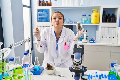 Young hispanic woman doing weed oil extraction at laboratory looking at the camera blowing a kiss being lovely and sexy. love expression.