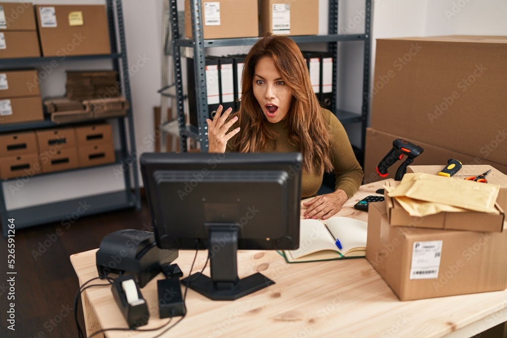 Hispanic woman working at small business ecommerce doing video call scared and amazed with open mouth for surprise, disbelief face Hispanic woman working at small business ecommerce doing video call scared and amazed with open mouth for surprise, disbelief face
