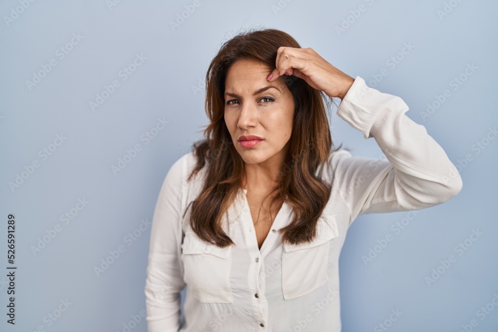 Hispanic woman standing over isolated background pointing unhappy to pimple on forehead, ugly infection of blackhead. acne and skin problem Hispanic woman standing over isolated background pointing unhappy to pimple on forehead, ugly infection of blackhead. acne and skin problem