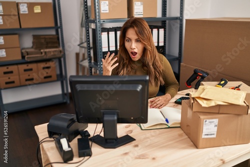 Hispanic woman working at small business ecommerce doing video call scared and amazed with open mouth for surprise, disbelief face © Krakenimages.com