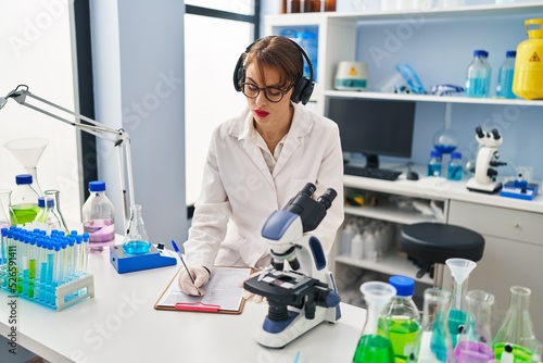 Young caucasian woman wearing scientist uniform listening to music working at laboratory