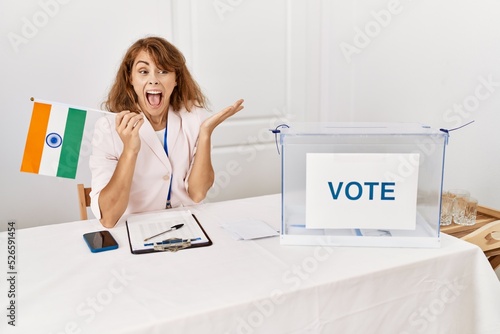 Beautiful caucasian woman at political campaign election holding india flag celebrating victory with happy smile and winner expression with raised hands