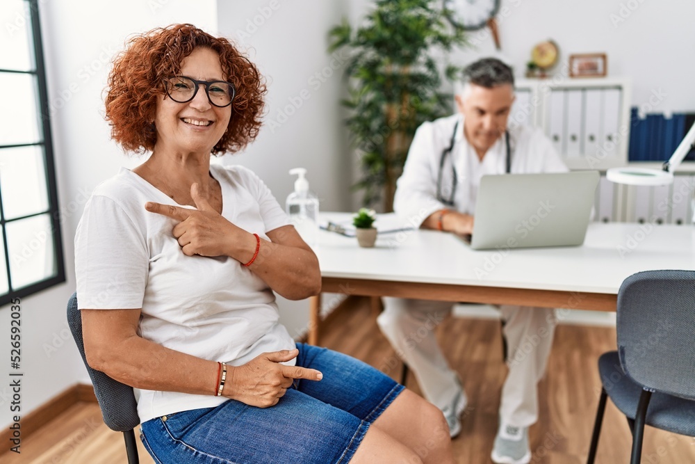 Senior woman sitting at doctor appointment cheerful with a smile of face pointing with hand and finger up to the side with happy and natural expression on face