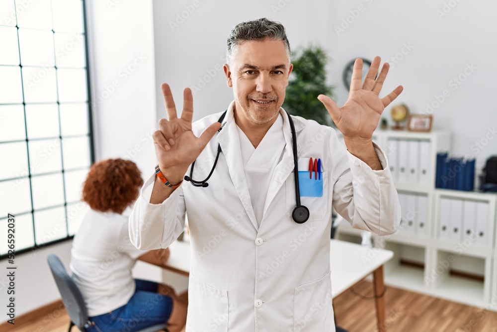 Middle age doctor man at the clinic with a patient showing and pointing up with fingers number eight while smiling confident and happy. Middle age doctor man at the clinic with a patient showing and pointing up with fingers number eight while smiling confident and happy.