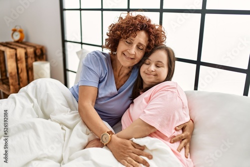 Mother and down syndrome daughter relaxing confortable on the bed hugging with love