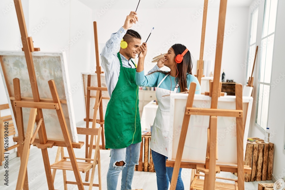 Young latin painter couple smiling happy painting and using headphones at art studio Young latin painter couple smiling happy painting and using headphones at art studio