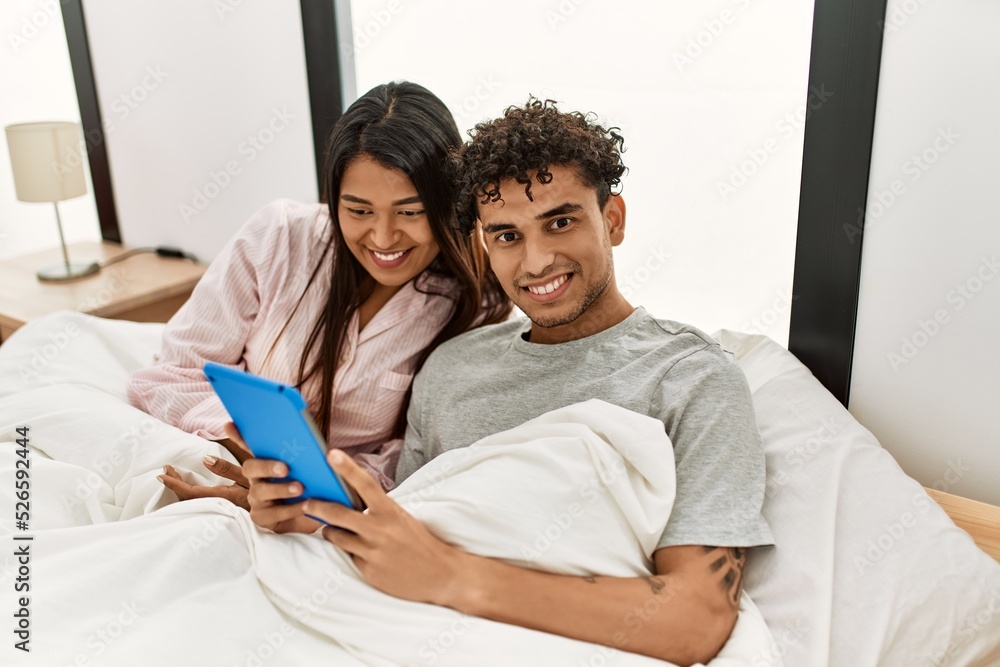 Young latin couple smiling happy using touchpad lying on the bed at bedroom. Young latin couple smiling happy using touchpad lying on the bed at bedroom.