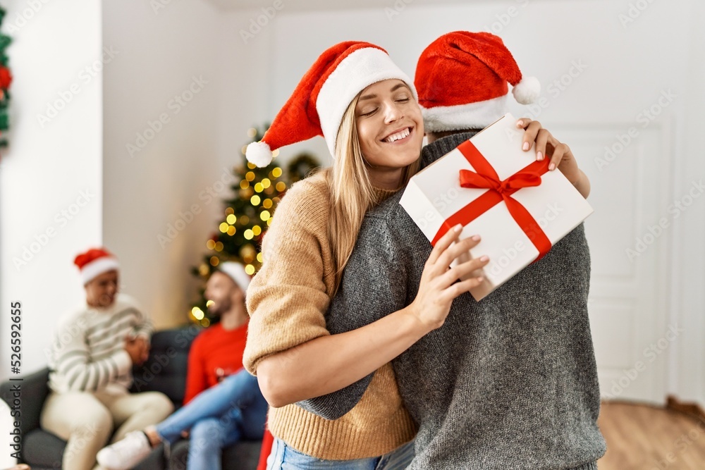 Fototapeta premium Group of young people on christmas meeting. Couple holding gift and hugging at home.