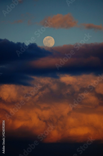 Interesting photo of a full moon above layers of heavy colorful evening clouds 