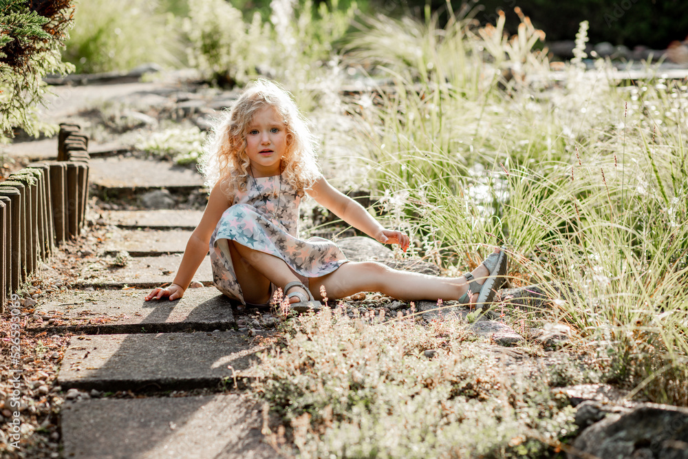 Portrait of poor crying awesome little girl with long fluffy curly hair wearing dress with stars, sitting after falling. Portrait of poor crying awesome little girl with long fluffy curly hair wearing dress with stars, sitting after falling.