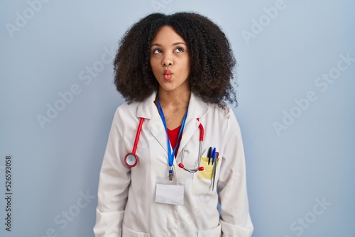 Young african american woman wearing doctor uniform and stethoscope making fish face with lips, crazy and comical gesture. funny expression.