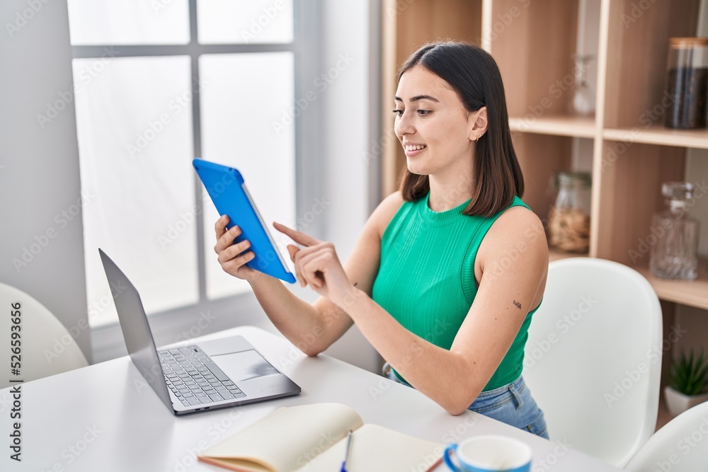 Young hispanic woman using touchpad sitting on table at home Young hispanic woman using touchpad sitting on table at home