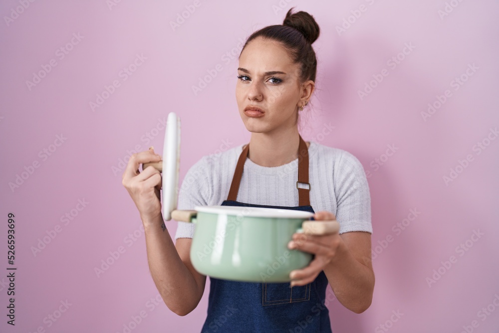 Young hispanic girl wearing apron holding cooking pot skeptic and nervous, frowning upset because of problem. negative person. Young hispanic girl wearing apron holding cooking pot skeptic and nervous, frowning upset because of problem. negative person.