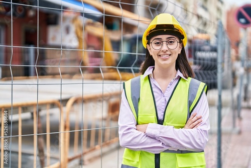 Young hispanic woman architect standing with arms crossed gesture at street
