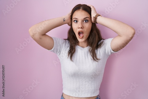 Young hispanic girl standing over pink background crazy and scared with hands on head, afraid and surprised of shock with open mouth