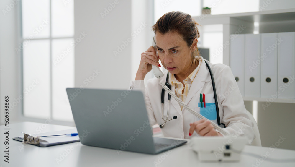 Middle age hispanic woman wearing doctor uniform talking on the telephone at clinic Middle age hispanic woman wearing doctor uniform talking on the telephone at clinic
