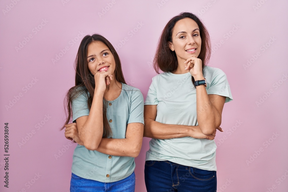 Young mother and daughter standing over pink background with hand on chin thinking about question, pensive expression. smiling and thoughtful face. doubt concept. Young mother and daughter standing over pink background with hand on chin thinking about question, pensive expression. smiling and thoughtful face. doubt concept.
