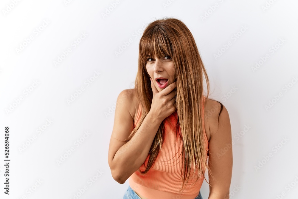 Hispanic woman with bang hairstyle standing over isolated background looking fascinated with disbelief, surprise and amazed expression with hands on chin Hispanic woman with bang hairstyle standing over isolated background looking fascinated with disbelief, surprise and amazed expression with hands on chin